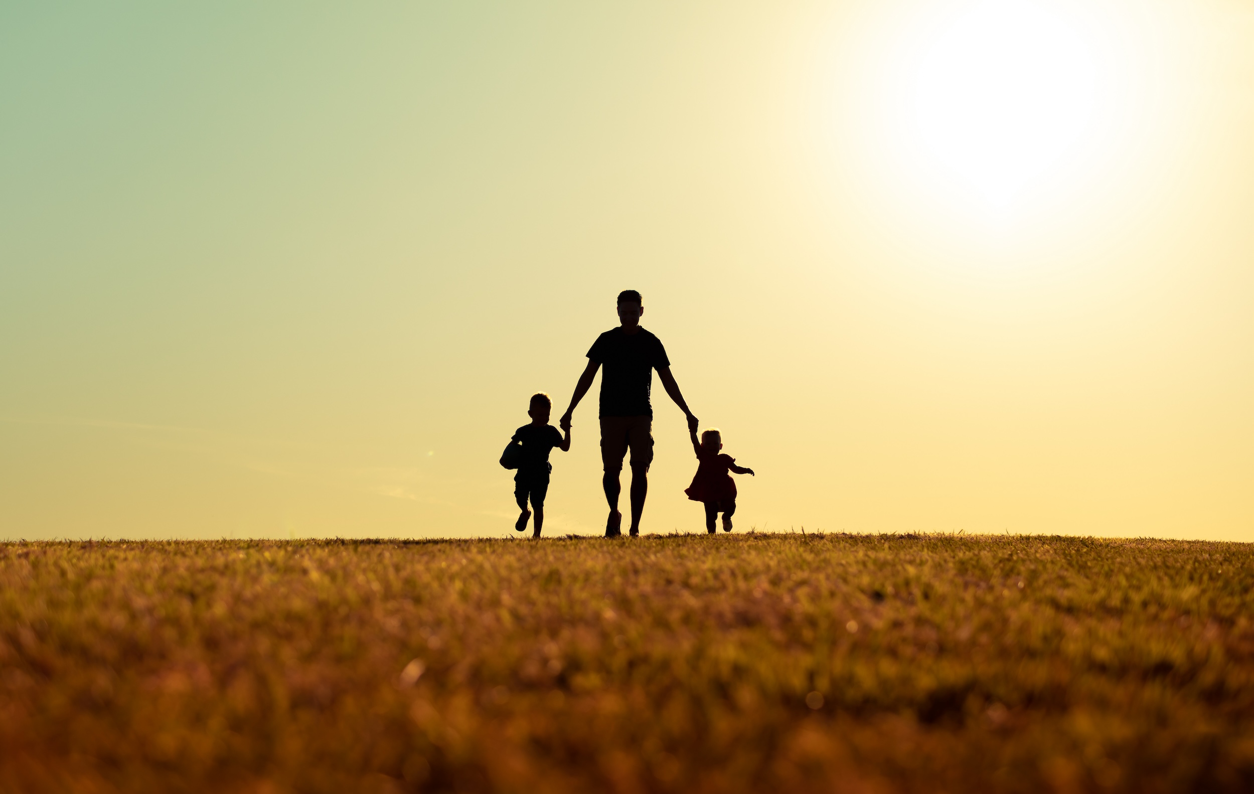 Father walking with son and daughter in park at sunset. fathers-day